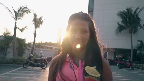 girl holds drink in hand smiling by hotel at back sunshine