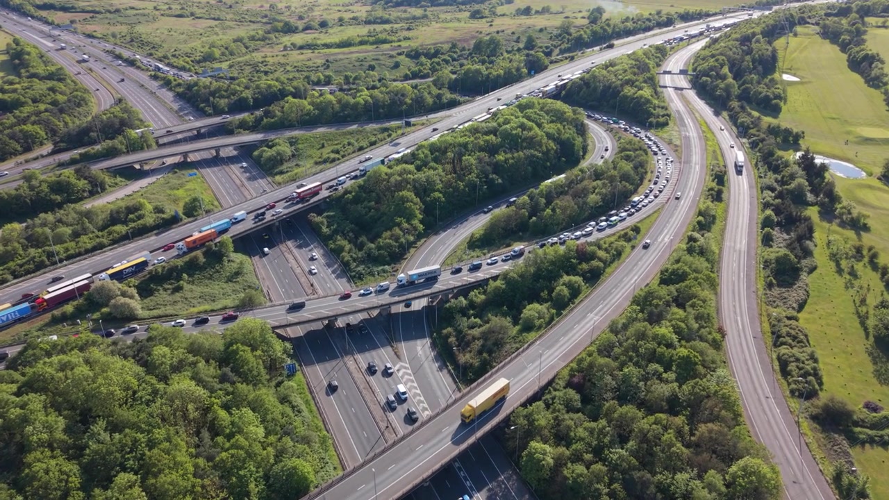 Overhead view of a busy multi-level highway interchange. Numerous cars, trucks, and buses are moving on the roads.