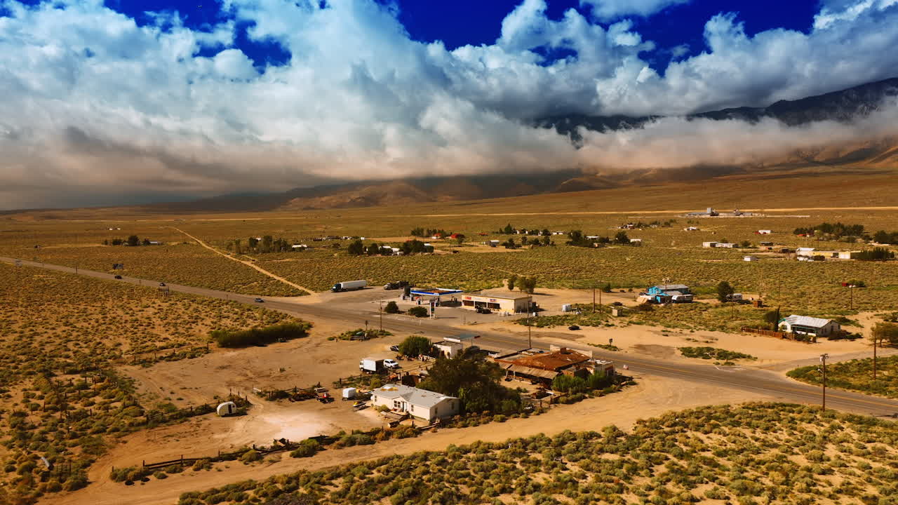Approaching the village in the desert of Death Valley, California. Some households are scattered in the area around the highway. Mountains hidden by clouds at backdrop.