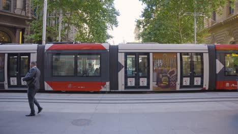 commuters walking by, as the tram goes by in downtown sydney, australia during rush hour