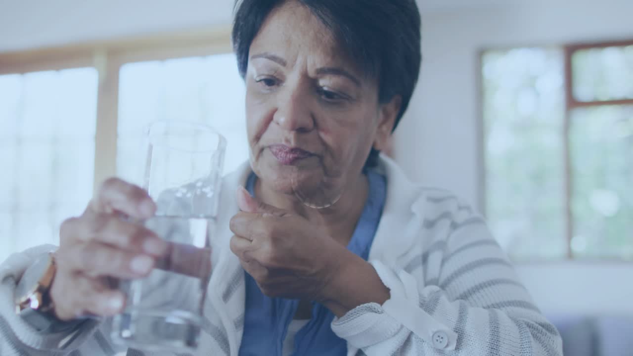 Senior woman scooping pills into palm and placing them on tongue then sipping water for medication