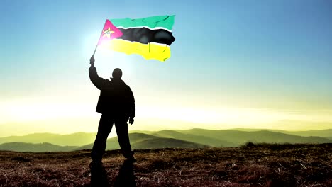 hombre ganador de silueta exitosa agitando la bandera de mozambique en la cima de la montaña, fondo de bucle de cinemagraph