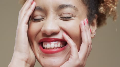 Happy-biracial-woman-with-dark-hair-and-red-lips-and-nails-on-beige-background,-slow-motion