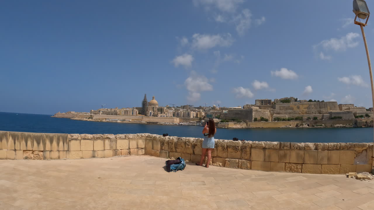 Una signora è in piedi su un muro che si affaccia sulla penisola con la città di La Valletta a Malta
