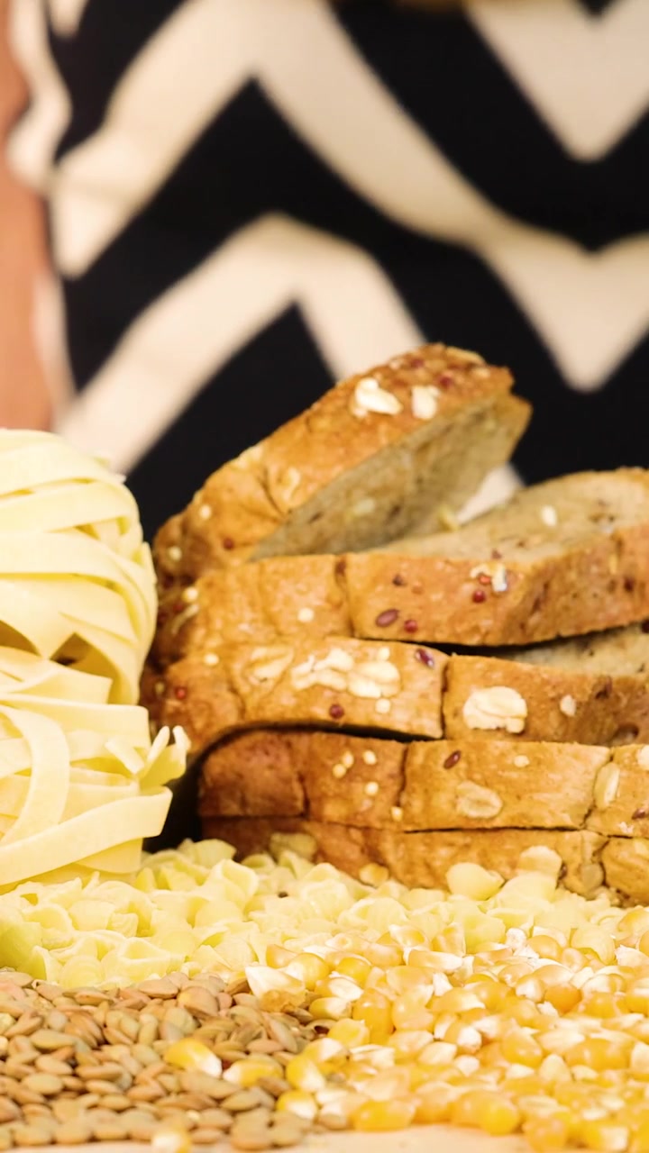 Mani organizzano con cura fette di pane integrale tra pasta, mais e lenticchie su un tavolo.