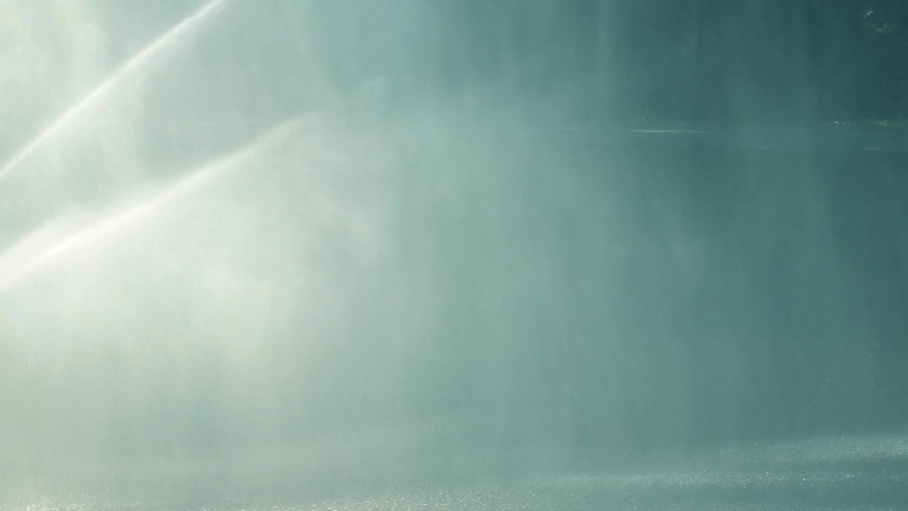 Close-up of fountain water jets spraying upward in dark blue light, with mist, motion, reflections, and an abstract aquatic atmosphere.