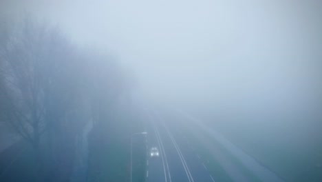 an aerial video of a road covered with mystical fog in the dark and cars passing along it