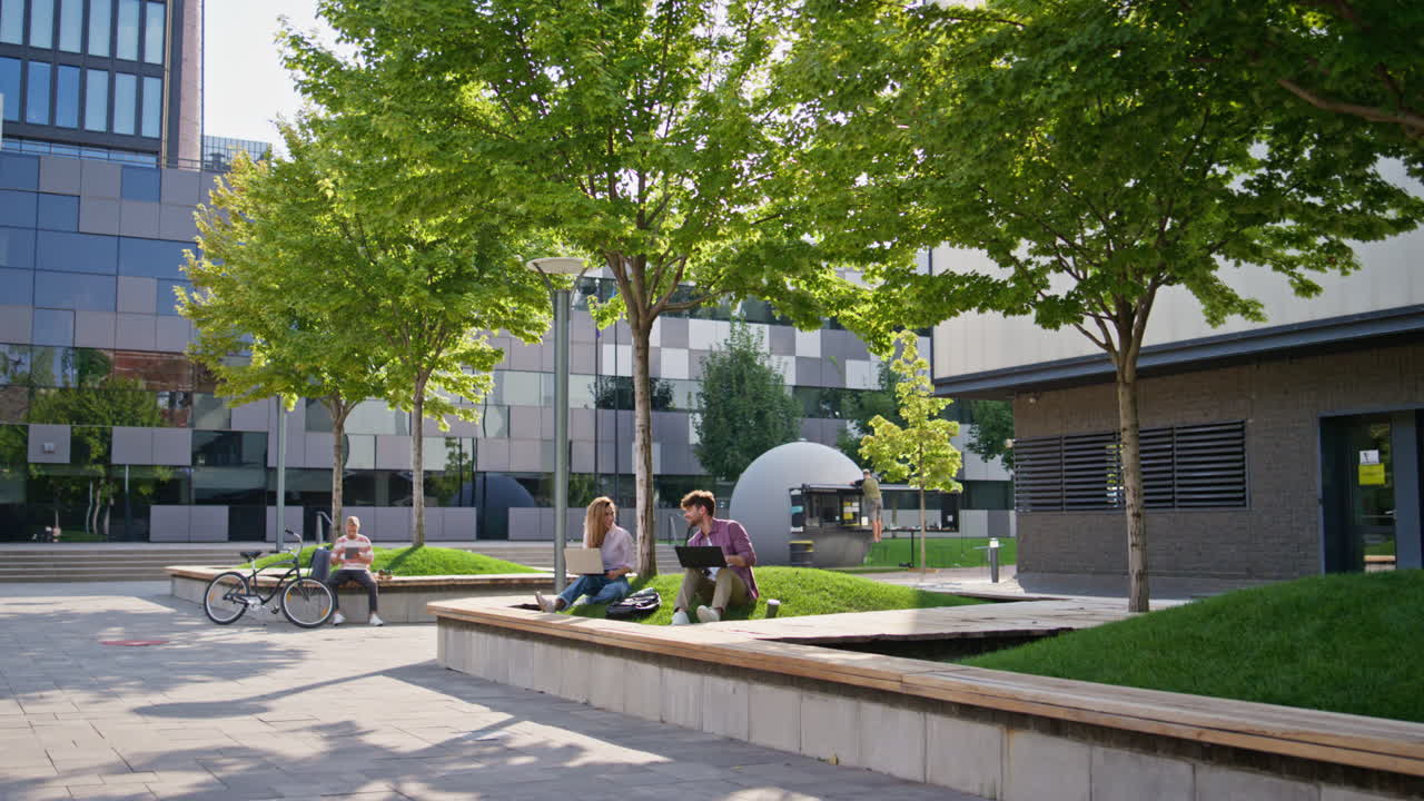 Casual people working outdoors at modern office building. Students study in park