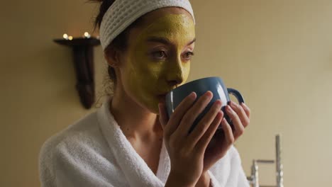 mujer biracial relajada con máscara facial bebiendo café