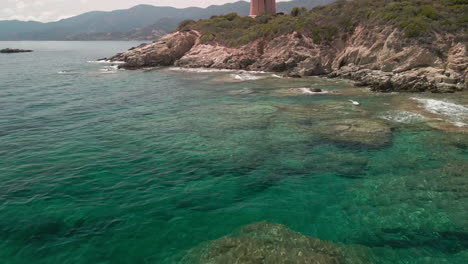 Aguas-Tranquilas-Del-Mar-Azul-Tropical-De-Cerdeña-Con-Vistas-Al-Acantilado-Y-Al-Antiguo-Puesto-De-Avanzada-En-La-Parte-Superior-Durante-Un-Día-Soleado-En-Italia---Toma-Aérea-De-Drones