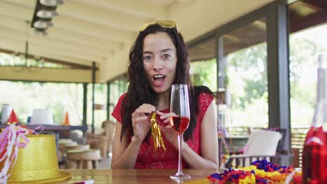 happy biracial woman with vitiligo making new year video call, holding wine and whistle