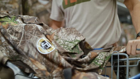 man putting hunting clothes in his cart at a retail store, then pushing the cart out of frame