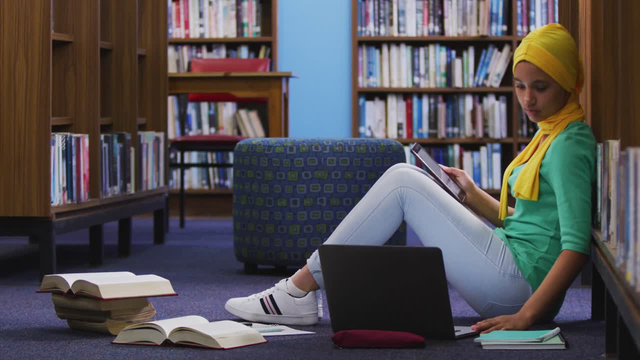 Asian female student wearing a yellow hijab sitting and using laptop