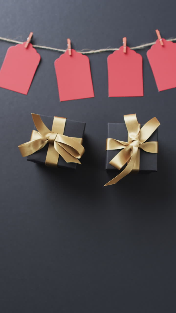 Vertical video of gift tags on string, gift boxes with ribbons and copy space on black background