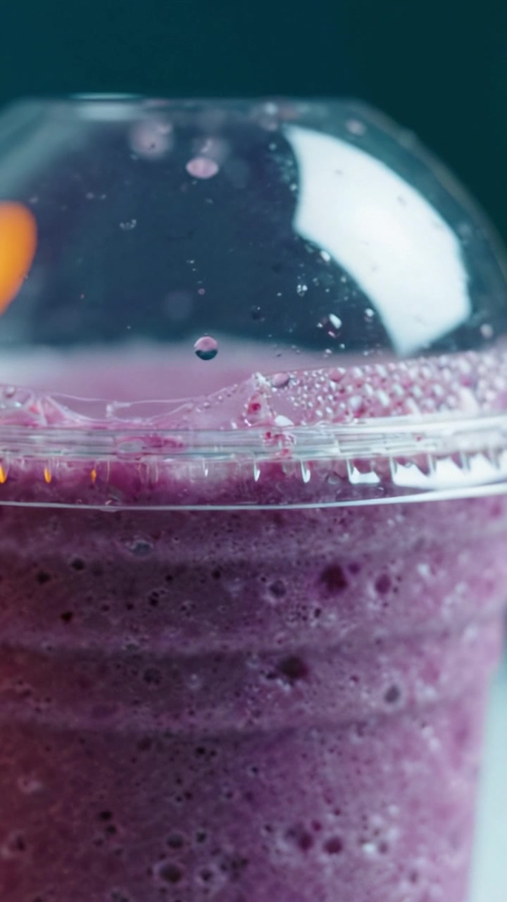 Un primo piano di una rinfrescante bevanda viola in una tazza trasparente con bollicine e goccioline, perfetta per le giornate calde e per dissetarsi.