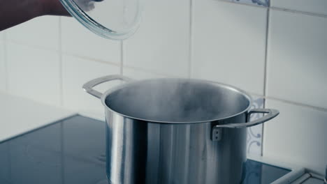 Primer-Plano-De-La-Mano-De-Una-Mujer-Abriendo-La-Tapa-De-Una-Gran-Olla-De-Hierro-Con-Agua-Hirviendo-Y-Humeante-Burbujeando-En-La-Estufa-De-La-Cocina-En-Cámara-Lenta