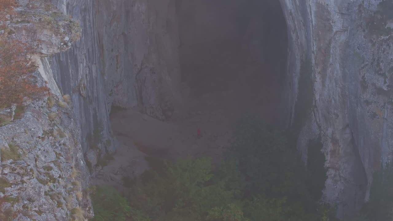 Mist rolls across cave opening and forest slopes, Bulgaria