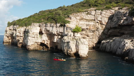 People-Kayaking-On-Blue-Water-Near-Cliffs-In-Pula,-Istria,-Croatia---aerial-drone-shot