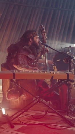 man plays igil and sings old fold song on stage with wooden logs. shamanic ceremony and throat singing at festival. traditions of altai art