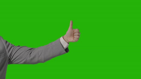 close up of arm of businessman in suit giving thumbs up gesture against green screen 1