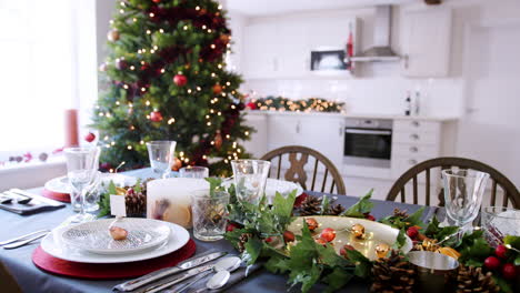 Una-Mesa-De-Comedor-Navideña-Festiva-Con-Un-Titular-De-Tarjeta-De-Nombre-De-Chuchería-Dispuesta-En-Un-Plato-Y-Decoraciones-De-Temporada-Verde-Y-Rojo,-Vista-Elevada