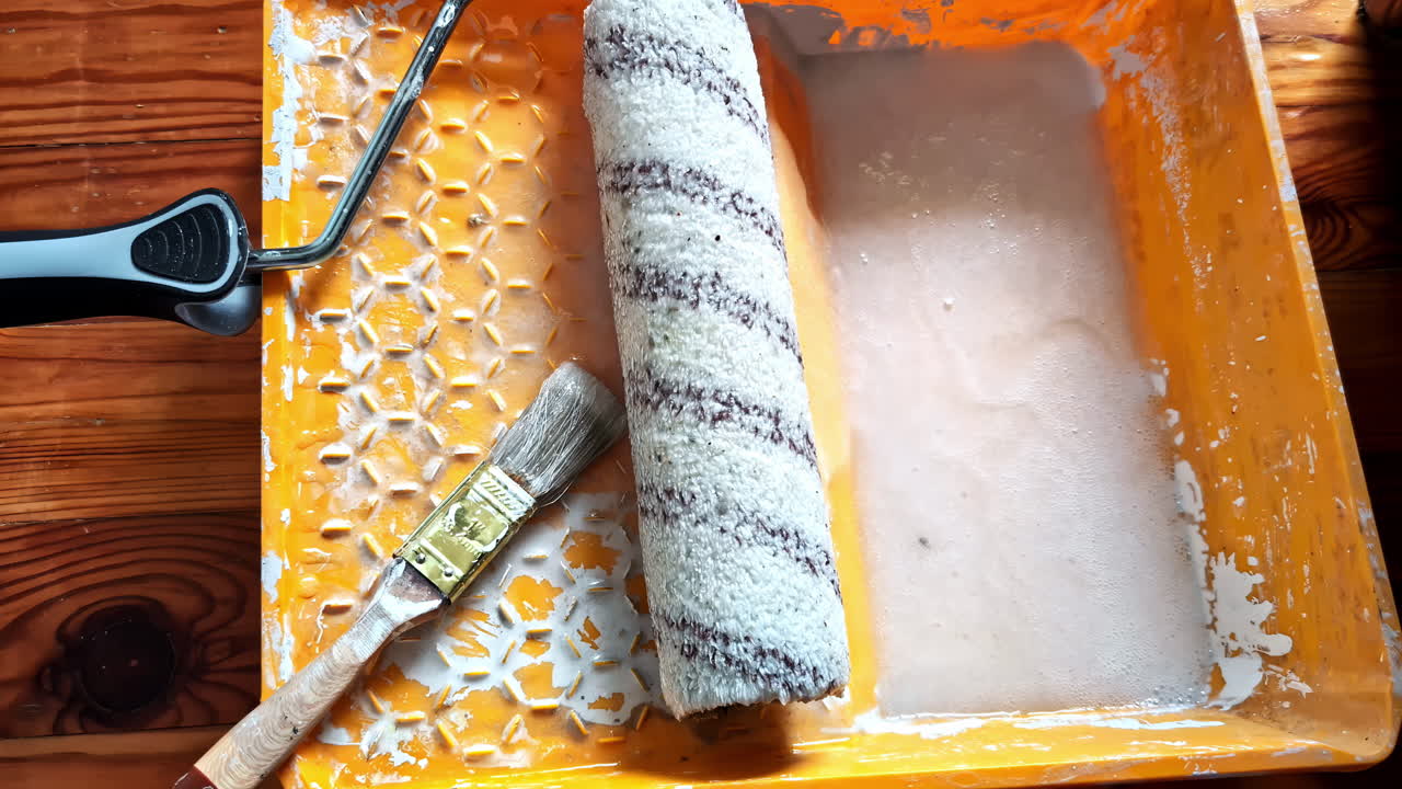 Wallpaper glue in tray with roller and brush on wooden floor