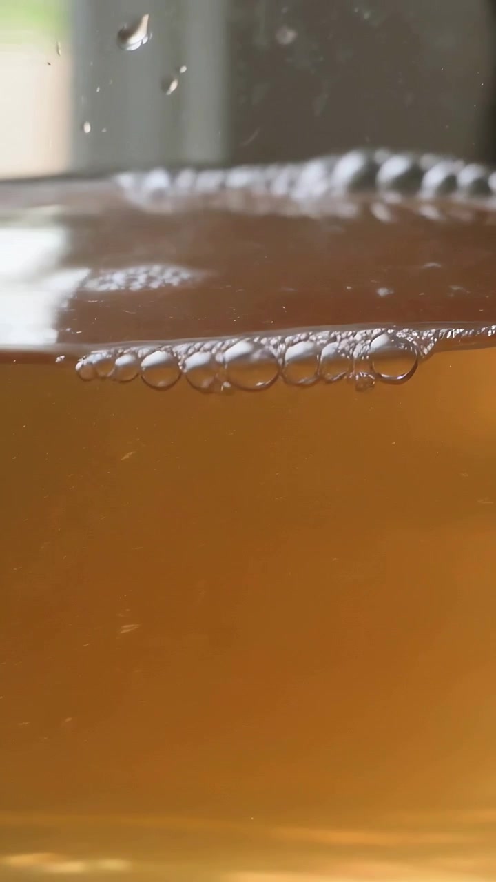 Video verticale: Mostra un barattolo di liquido ambrato che forma bolle a causa delle increspature a casa mentre l'inquadratura si allontana.