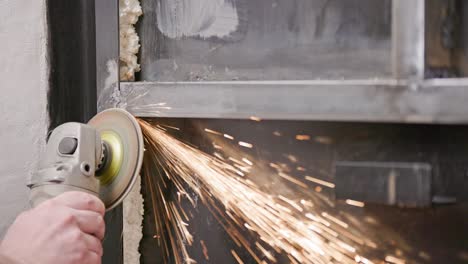 caucasian hand cleaning of welded seams with an angle grinder with a flap disc on welded metal construction close-up with long spark trails, slow motion