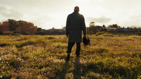 elderly man holding an umbrella walks toward the sun on a meadow