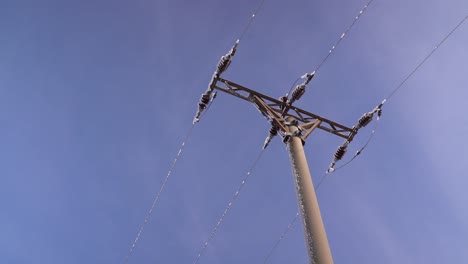 looking up at utility pole with snow falling off against blue sky