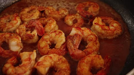 extreme close up shot of delicious peeled shrimps, simmering and boiling on hot pan, reducing and absorbing the juicy flavours of red paprika spice, cooking seafood cuisine