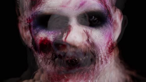 unheimlicher mann mit schrecklich beängstigendem halloween-zombie-make-up in krämpfen, der gesichter macht, um zu erschrecken