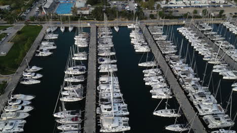 Drone-captures-a-stunning-orbital-shot-of-a-Greek-port-filled-with-white-sailboats,-highlighting-the-contrast-between-the-dark-water-and-the-white-sailboats