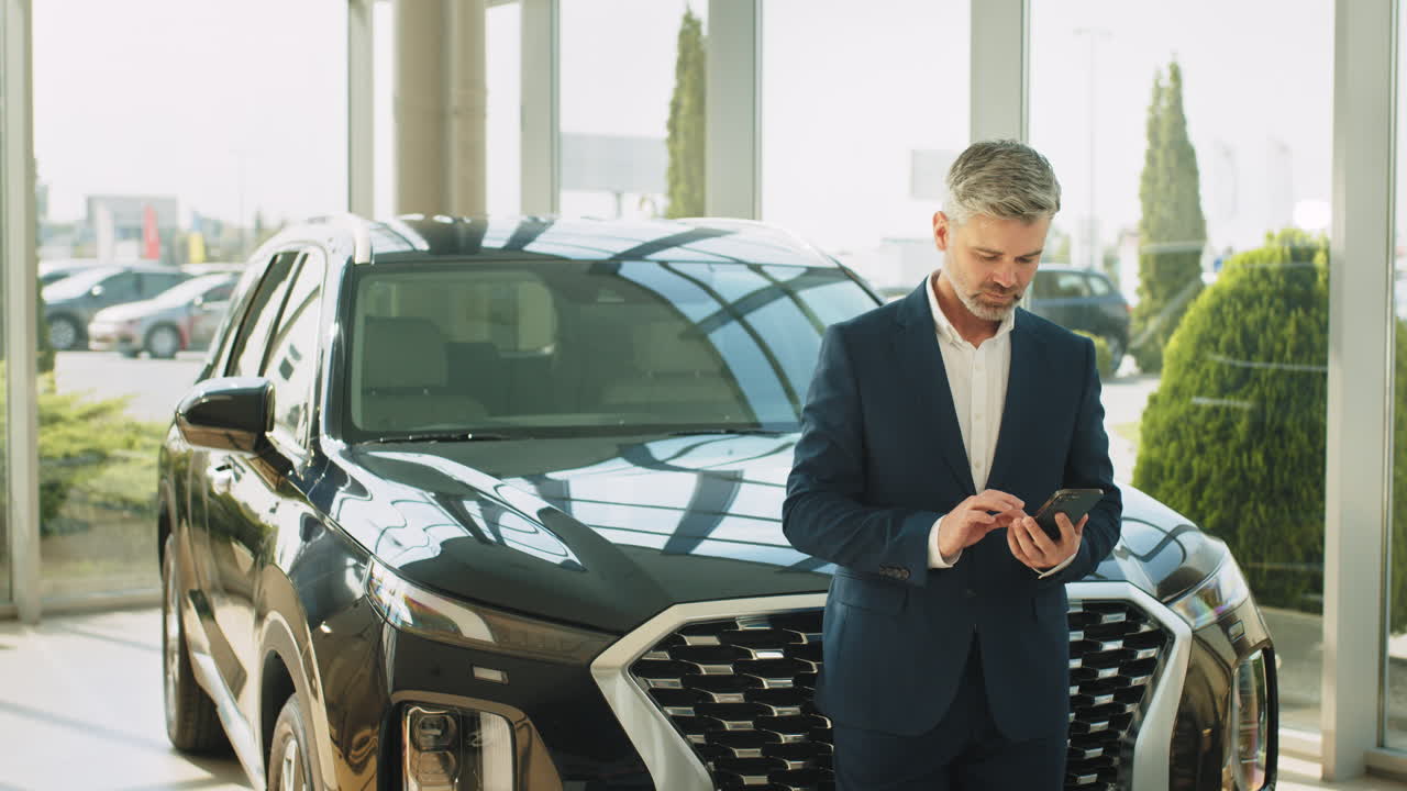 hombre de negocios mirando un teléfono inteligente frente a un suv negro en una sala de exposición de automóviles