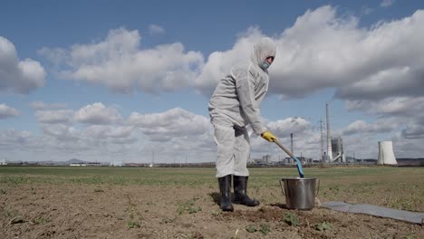 laboratory assistant in protective workwear digging ground with shovel and bucket for soil sampling