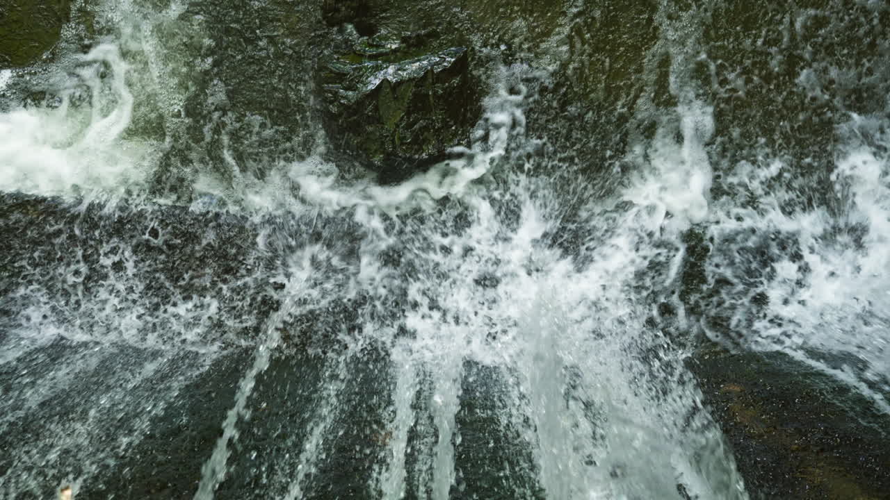 Waterfall from a dam goes into the river in slow motion and the water in splashing when it hits the stone and the concrete