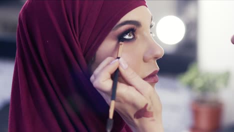 adding some more eyeliner on the waterline of a gorgeous girl's eyes. stunningly beautiful female wearing purple hijab