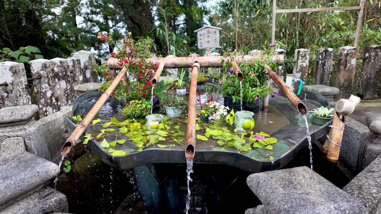 Water pouring from bamboo pipes into stone basin of nachisan water fountain, decorated with flowers, leaves and fruits