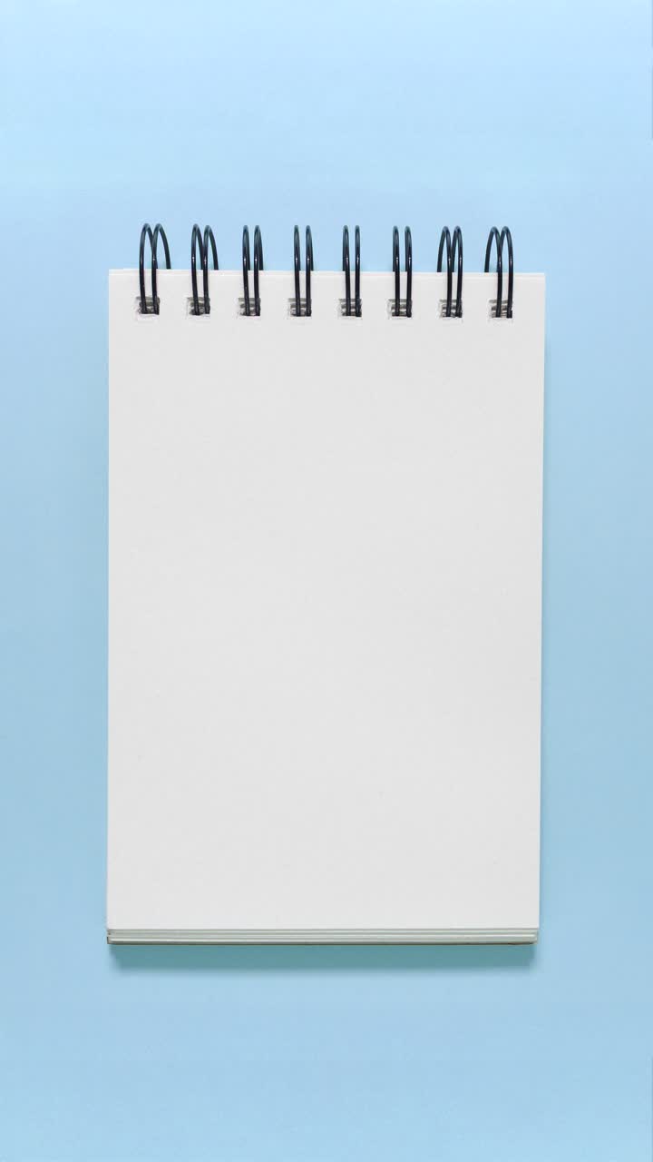 Portrait stop motion of a blank spiral sketchbook sliding in from the side on blue, leaving clean copy space