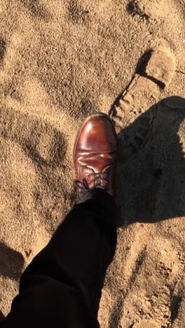 elegant man walking on sand: close up of leather shoes on beach