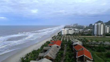 Impresionante-Sobrevuelo-De-Una-Playa-Bang-En-Vietnam-Mientras-Las-Olas-Golpean-La-Playa-De-Arena-Y-La-Exuberante-Vegetación