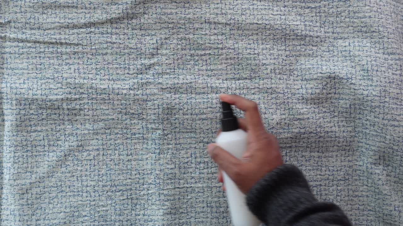 스프레이 병을 들고 천 표면을 스프레이하는 사람의 손