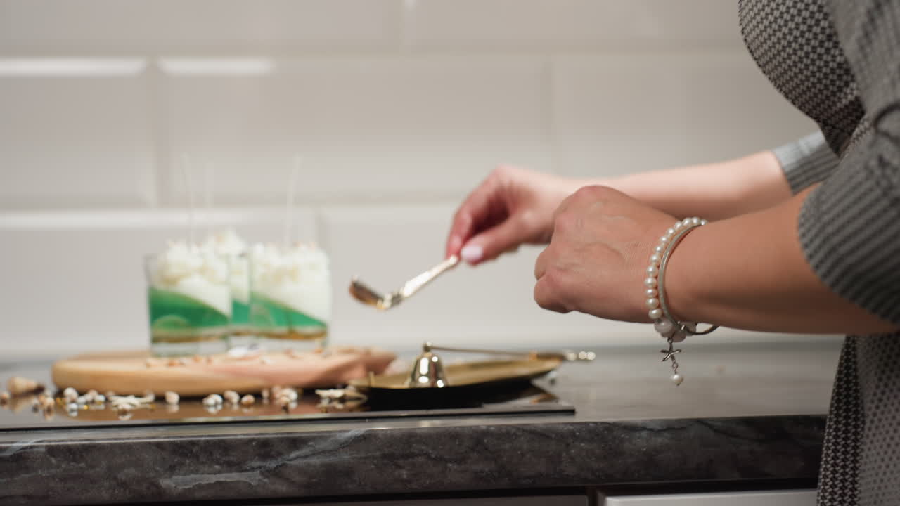 Fair skinned woman in checkered dress lifting golden spoon from golden tray with visible golden bell beside it, set on tiled kitchen background, capturing elegant domestic moment in motion