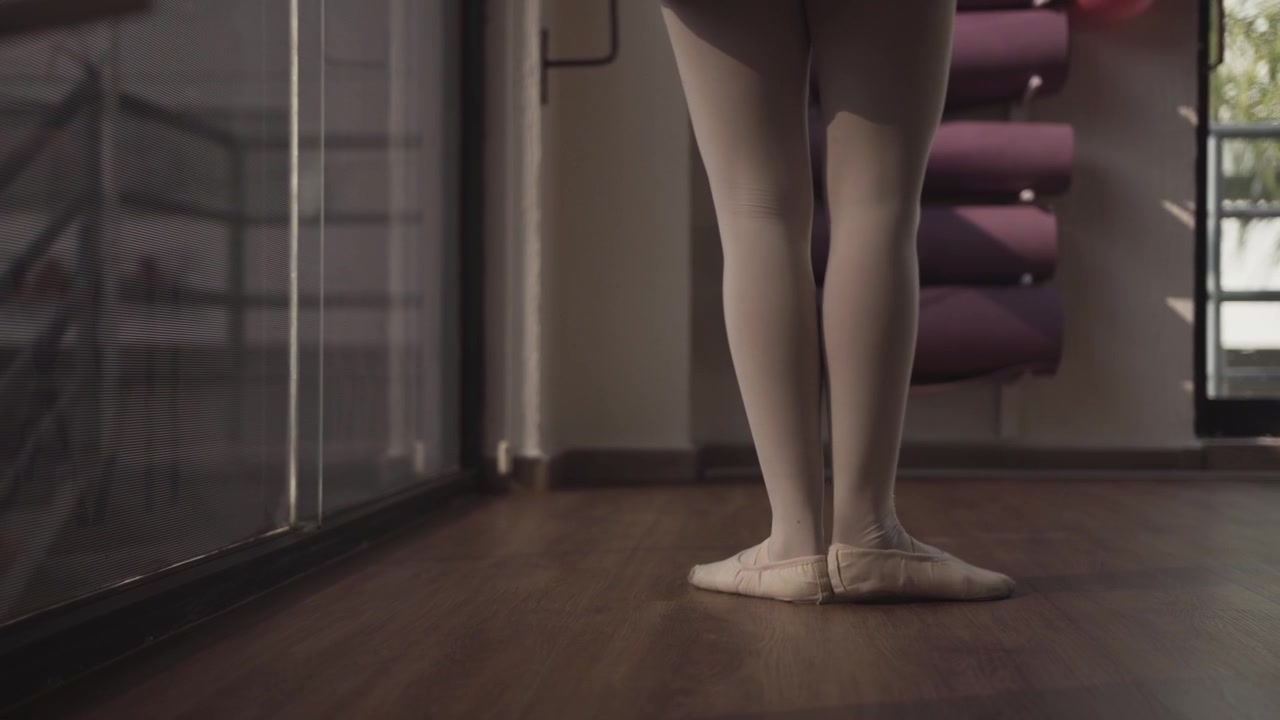 Primo piano di una ballerina che si riscalda con movimenti aggraziati dei piedi su un pavimento di legno prima della lezione di danza all'interno di uno studio moderno di giorno