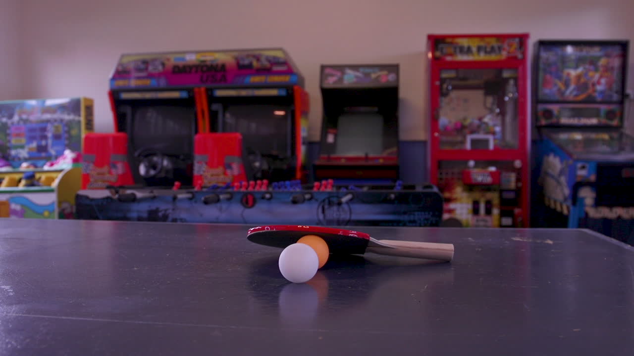 Una palla bianca che rotola e una racchetta rossa su una palla da ping pong arancione con giochi arcade sullo sfondo