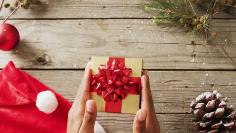 video of biracial woman holding christmas gift with christmas decoration on wooden background