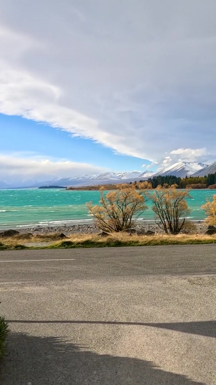 Una suggestiva prospettiva verticale di un vivace lago turchese, alberi autunnali e montagne innevate in lontananza.