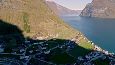 Toma-Aérea-De-Drones-En-Movimiento-Hacia-Atrás-De-Casas-De-Pueblo-A-Lo-Largo-De-La-Ladera-De-La-Montaña-Con-El-Paso-Del-Río-En-Noruega-Durante-Una-Mañana-Soleada