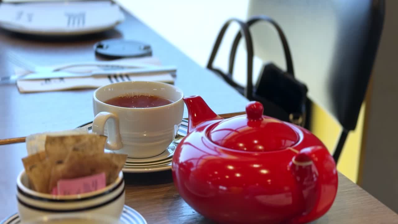 Steaming tea served in a white cup with matching saucer and red teapot on a cozy cafe table — ideal for food, beverage, lifestyle, and hospitality marketing