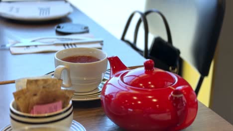 steaming tea served in a white cup with matching saucer and red teapot on a cozy cafe table — ideal for food, beverage, lifestyle, and hospitality marketing